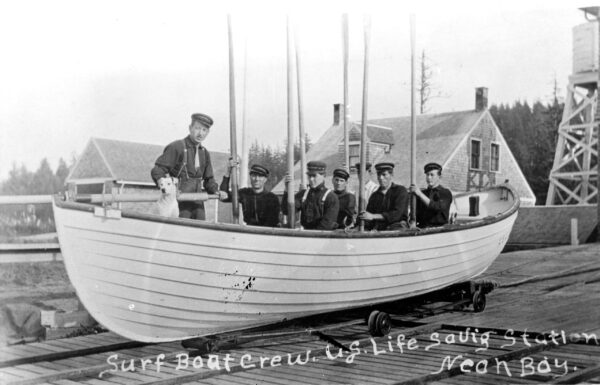Photo: Sailors in the U.S. Life-Saving Service posing in a boat in dry dock, holding their oars aloft and accompanied by their dog. Taken about 1910 the Black and white photograph with caption written on front reads: 