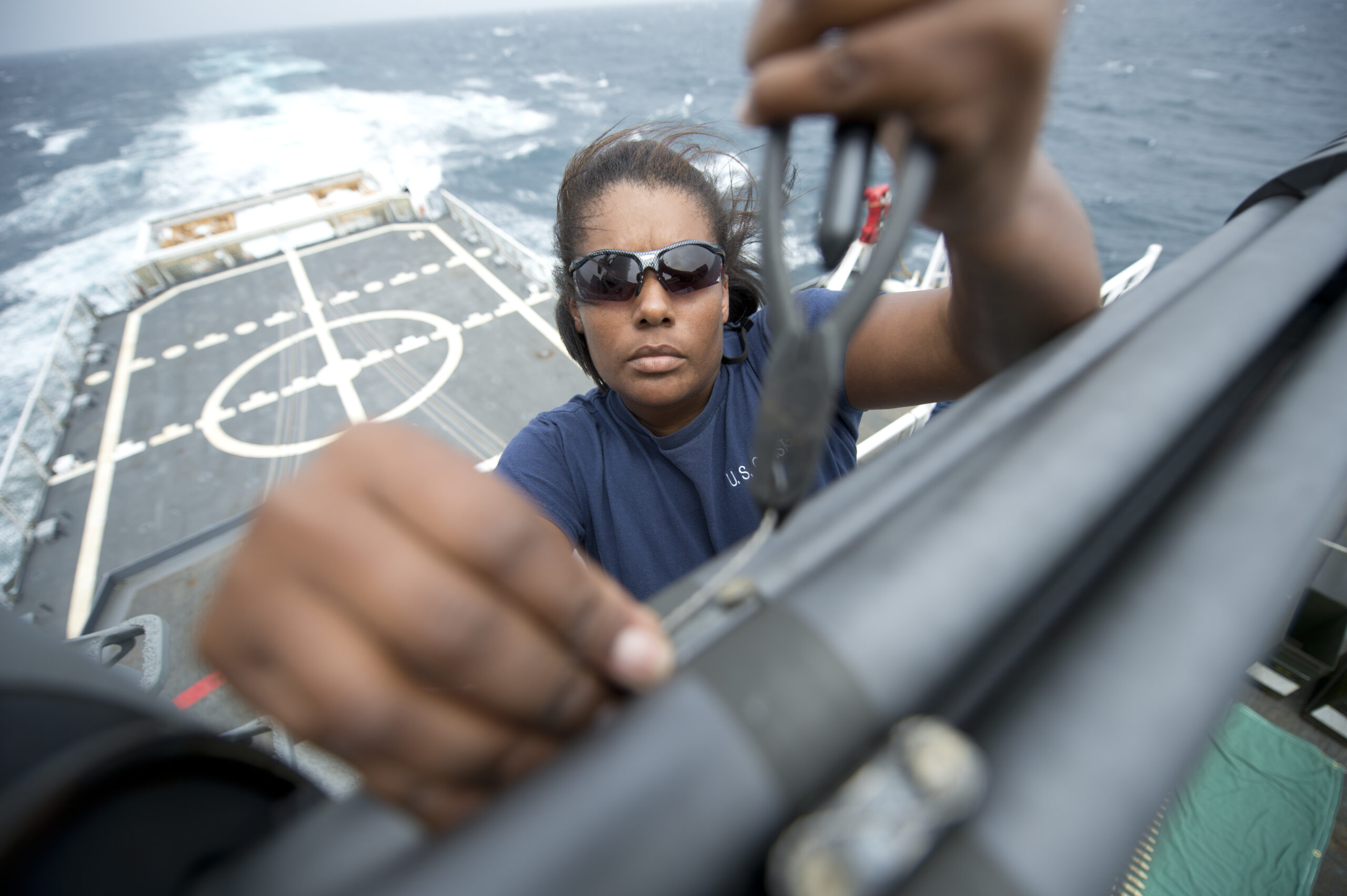 Color photograph of a female electronics technician standing high above the helicopter pad, working with tools.