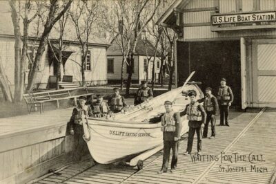 A photograph of the U.S. Life Saving Service crew posing with its surfboat in front of U.S. Life-Saving Station at St. Joseph, Michigan.