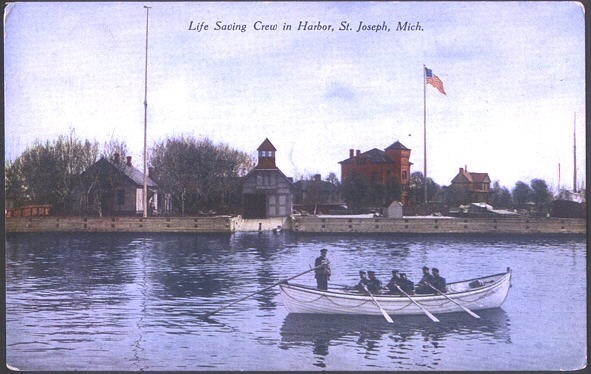 A colorized photograph/postcard showing the St. Joseph Station crew in its surfboat in front of the station boathouse on the St. Joseph waterfront.