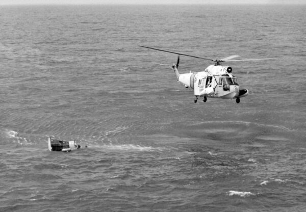 Photo: Coast Guard helicopter hovers over Gemini III space capsule floating on its side.
