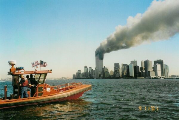 Photo: A Coast Guard rigid-hull inflatable boat with World Trade Center burning in background.