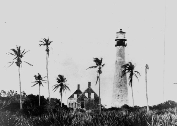 Photo of lighthouse in Florida accented by palm trees and a roofless house.