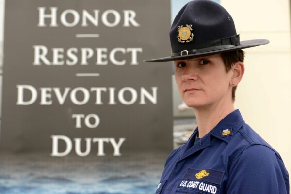 Photo: Petty Officer 1st Class Speece poses for a photo in front of the Coast Guard’s core values.