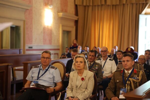 Photograph: Military and civilian delegates of many nations seated in a conference room.