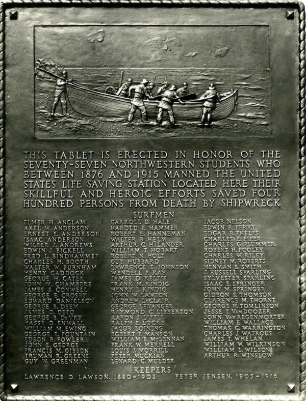 Plaque with the relief illustration of surfmen taking boat out to sea, followed by the following text: “This tablet is erected in honor of the seventy-seven northwestern students who between 1876 and 1915 manned the United States Life Saving Station located here their skillful and heroic efforts saved by four hundred persons from death by shipwreck” , then the name list of surfmen and keepers.