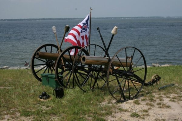 Photograph: two howitzer cannons displayed on the shore along with ordinance and a flag.