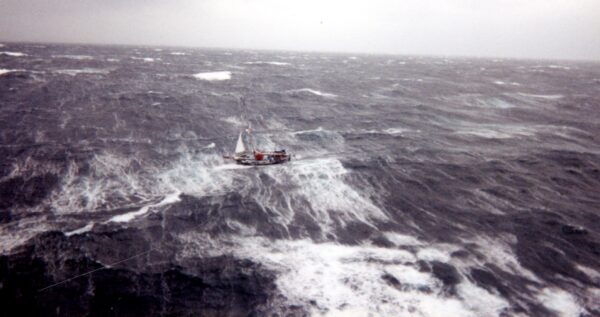 Photo: Color photograph of the sailboat Satori nearly submerged in massive, white-capped waves during the 1991 Perfect Storm.