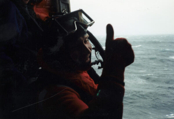 Photo: View from inside the helicopter of rescue swimmer over the ocean gives the thumbs up sign.