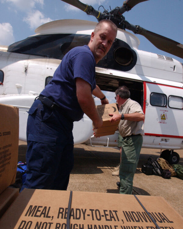 Photo: A Coast Guard member loads cases of meals, ready-to-eat (MREs) into a helicopter.