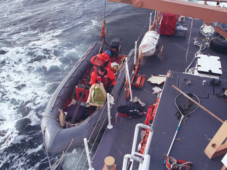 Photo: Crewmembers move recovered wreckage from their inflatable boat to the deck of a cutter.