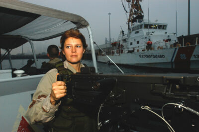 Photo: Boatswain's Mate Zora Tate stands behind her gun while her boat patrols the water around the USCGC Adak.