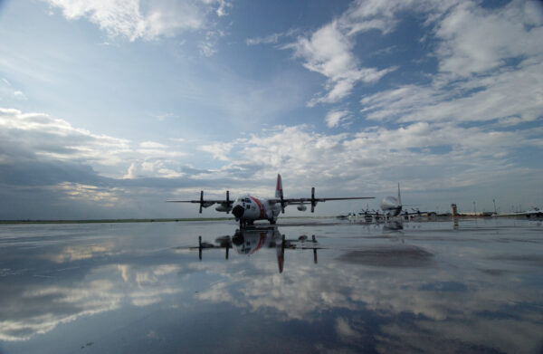 Photo: A Coast Guard C-130 stands on a wet mirror-like tarmac.