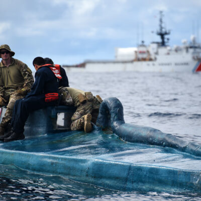 Photo: Coast Guard members sit on top blue camouflaged smuggling vessel sitting just at water level.