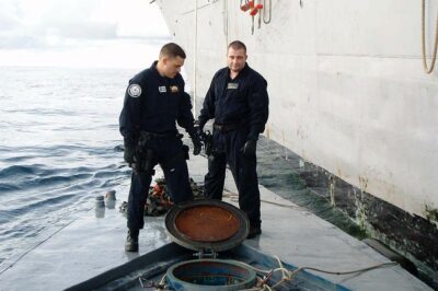 Photo: Two LEDET team members stand on top of a semi-submersible craft and look down into an open port.