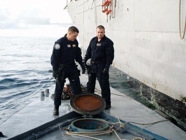 Photo: Two LEDET team members stand on top of a semi-submersible craft and look down into an open port.