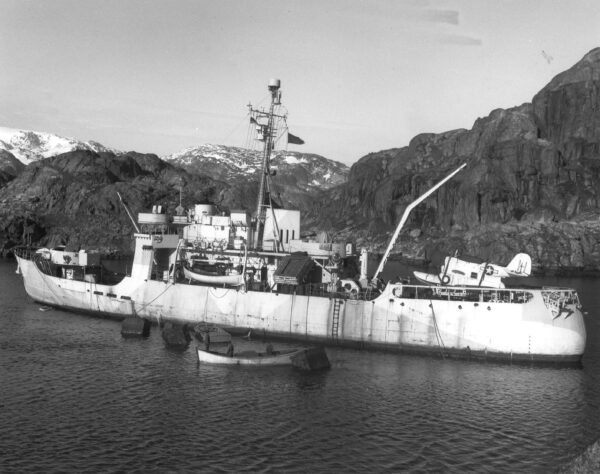 Photo: Storis displaying her deck and anti-aircraft guns, faded ice camouflage hull paint, as well as depth charge racks and a Grumman J2F “Duck” amphibian aircraft.