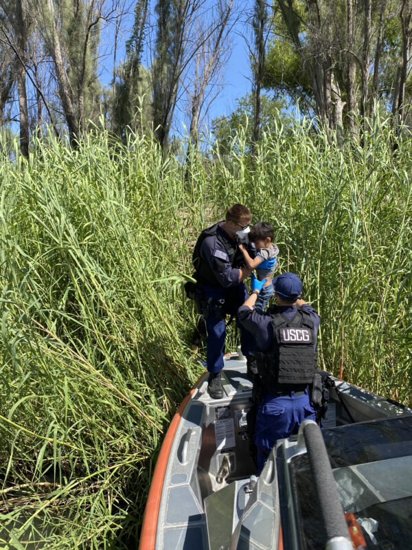 MSST member lifts a child from thick reeds on a riverbank.