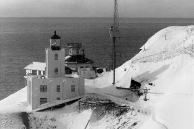 Winter-time photograph showing the old Scotch Cap Lighthouse located behind the new concrete lighthouse built in 1940.