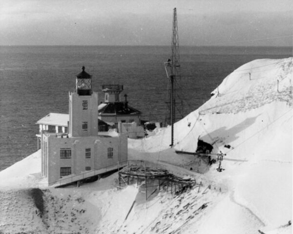 Winter-time photograph showing the old Scotch Cap Lighthouse located behind the new concrete lighthouse built in 1940.