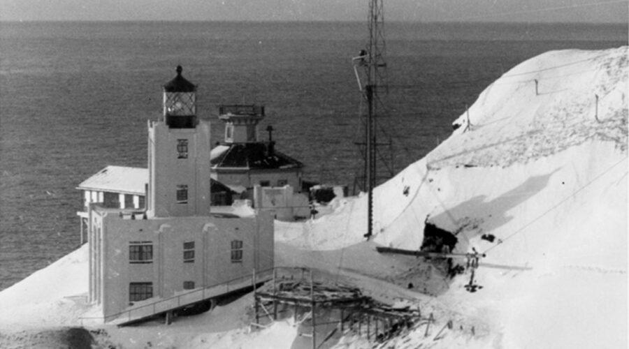 Winter-time photograph showing the old Scotch Cap Lighthouse located behind the new concrete lighthouse built in 1940.