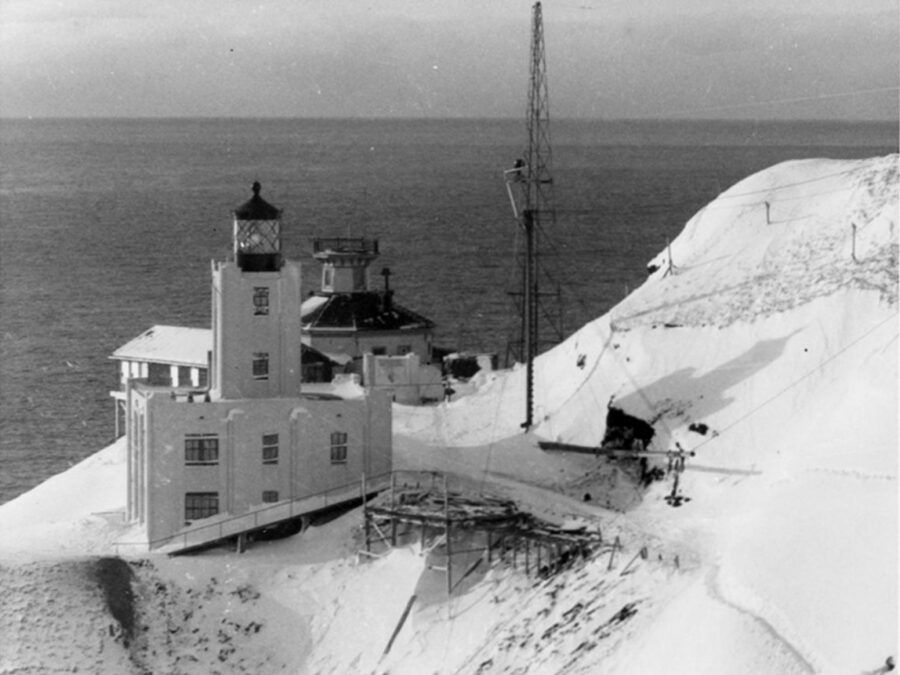 Winter-time photograph showing the old Scotch Cap Lighthouse located behind the new concrete lighthouse built in 1940.