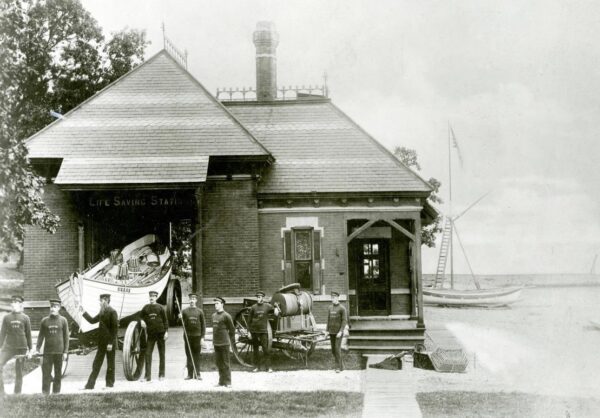 Period photograph of the Parkinson-designed 1877 station building, with the station’s Beebe type pulling surfboat on its boat wagon at left, and the beach cart at center. Keeper Lawson can be seen at the front of the surfboat.