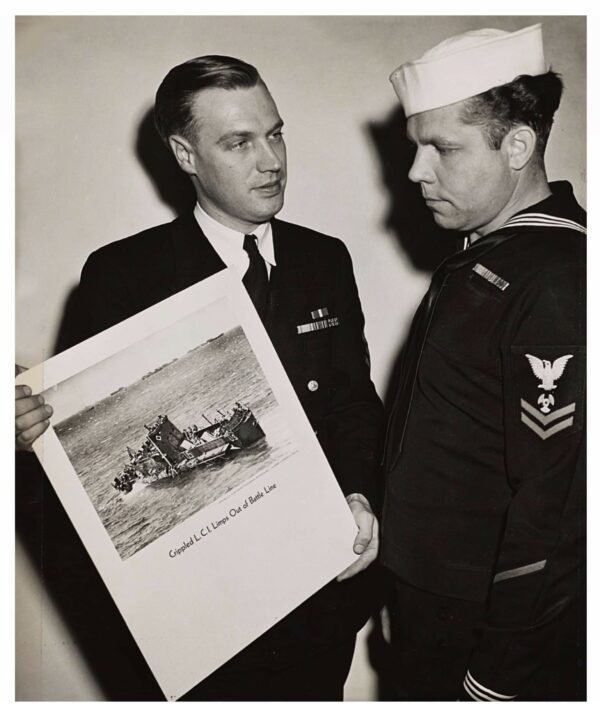 Photo: Coast Guard Chief Photographer’s Mate Robert Sargent (left) shows Coast Guard Motor Machinist’s Mate Clyde Wilson a picture of the battle-blasted Coast Guard-manned LCI that Wilson served on D-Day.