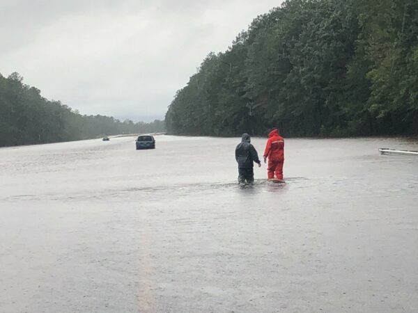 Photo: A Coast Guard team member stands with motorist on a flooded road.