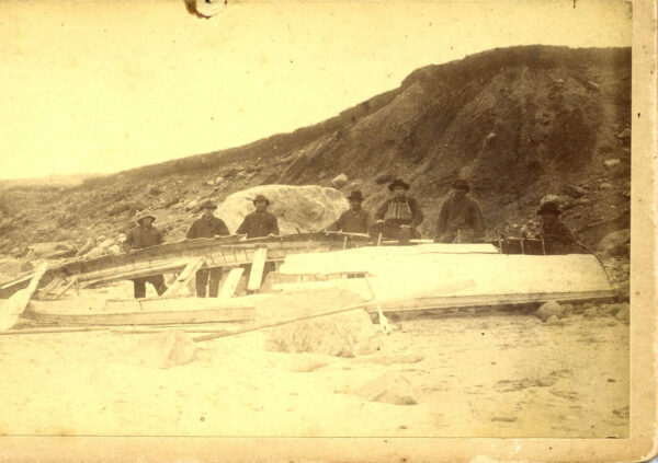 Photo: Men standing next to remains of a surfboat.