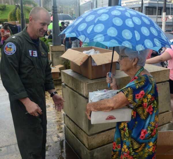 Photo: Cdr. Jeremy Anderson engages in conversation with elderly woman while delivering relief supplies.