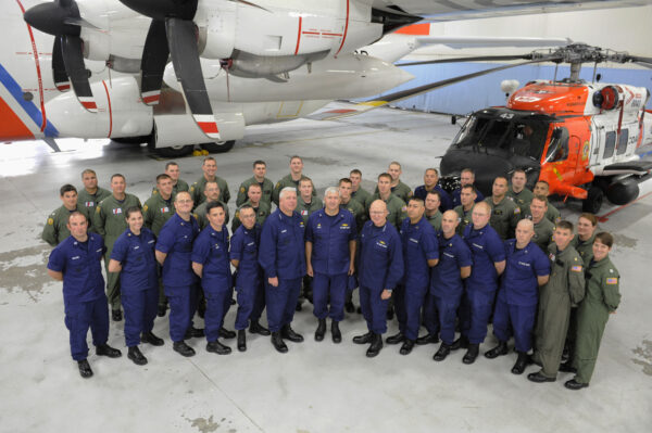 Photo: Air crews and leadership pose next to a helicopter and HC130 Hercules airplane.