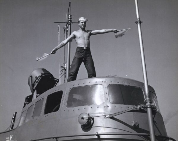 Photo: A shirtless signalman waves flags from the top his his Sub Buster.