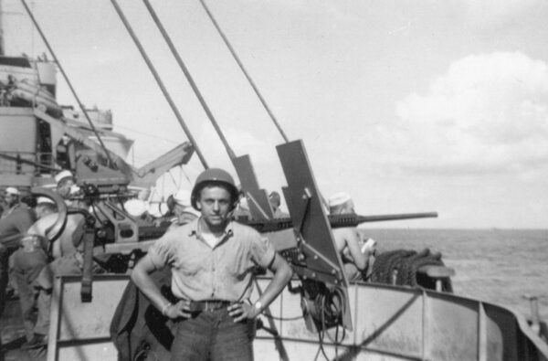 Photo: Frank DeVita standing in front of a 20mm gun mount on board the Samuel Chase.