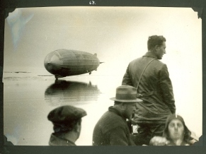 Photo: People in foreground, with Graf Zeppelin hovering over mirrorlike surface.