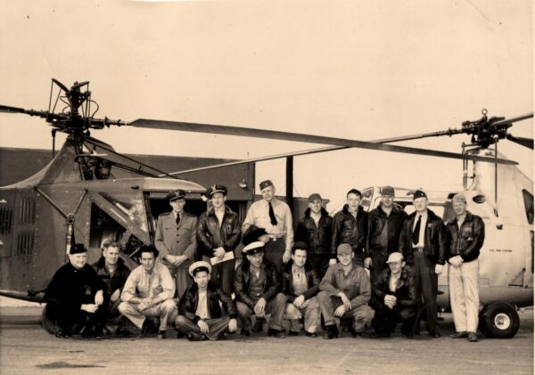 Sepia photo: 16 men in uniform pose inf front of two helicopters.