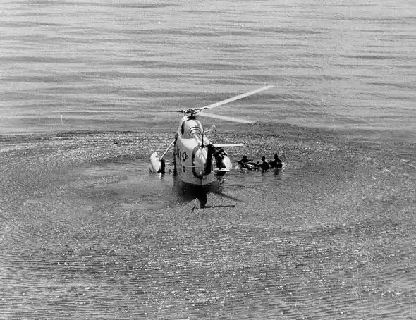 Photo: A Coast Guard HH-25 “Seaguard” helicopter making a water rescue, with three visible people in the water.