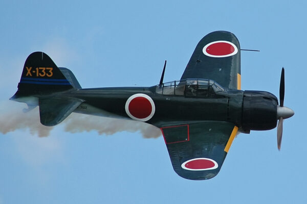 Photo: Japanese Zero fighter flying with smoke emanating from fuselage.