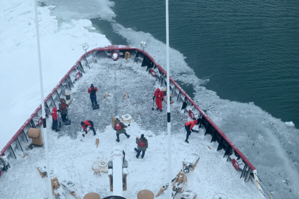 Photo: Overhead view of crewmembers working to clear ice and snow from the deck and equipment.
