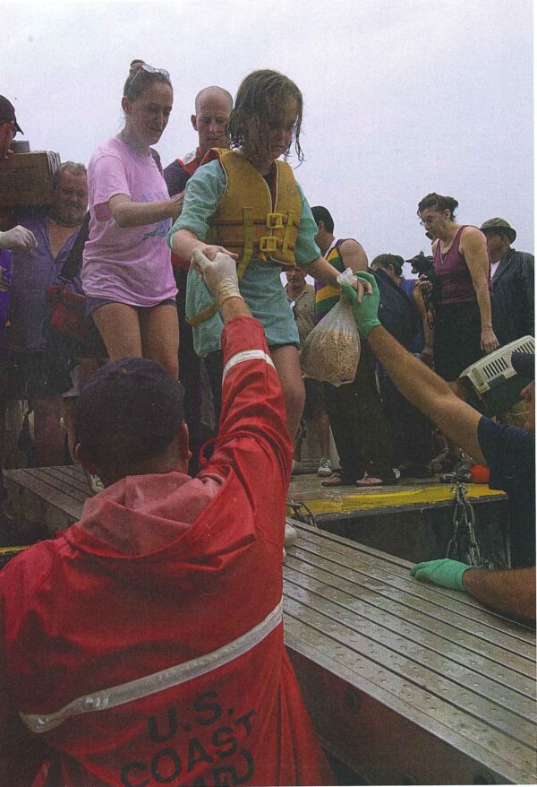 Photo: Coast Guard personnel assist displaced persons disembarking the evacuation barge.