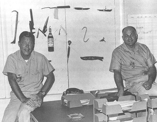 Photo: Two uniformed men sitting on desk.