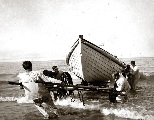 Photo: Men pulling surfboat ashore on wagon.