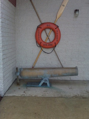 Photo: A 24-pound boat howitzer displayed with paddle, hook, and life preserver from Coast Guard Station Lake Erie.