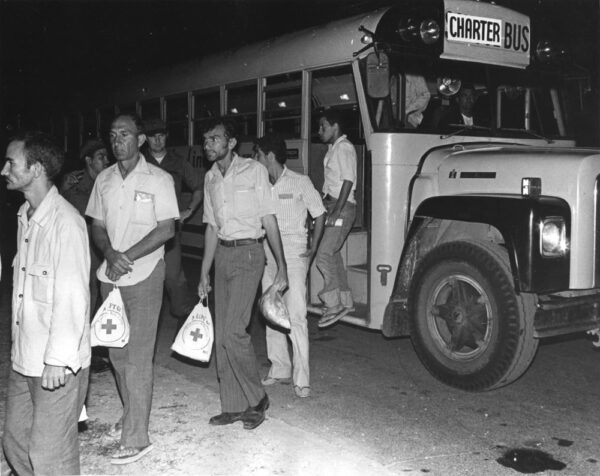 Photo: Refugees carrying Red Cross aid bags exit a charter bus.