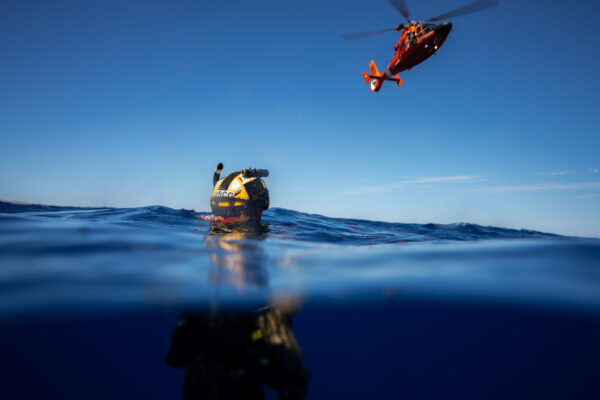 Photo: Rescue swimmer treads placid water while helicopter hovers overhead.