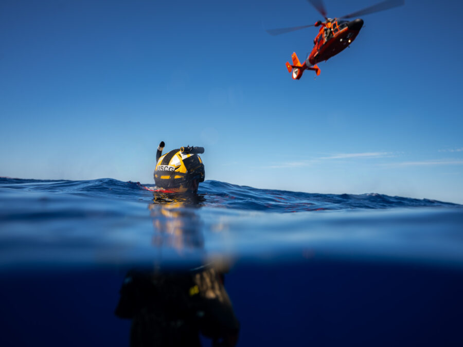 Photo: Rescue swimmer treads placid water while helicopter hovers overhead.