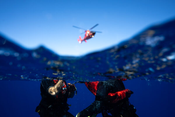 Photo: Underwater view of rescue swimmers training in water while helicopter hovers overhead.