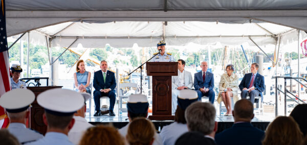Adm. Linda Fagan speaks at a podium, flanked by seated lawmakers and museum officials, to an outdoor gathering of guests for the keel-laying ceremony.