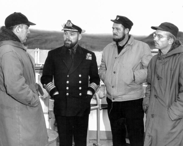 Photograph: Men in coats conferring on deck.