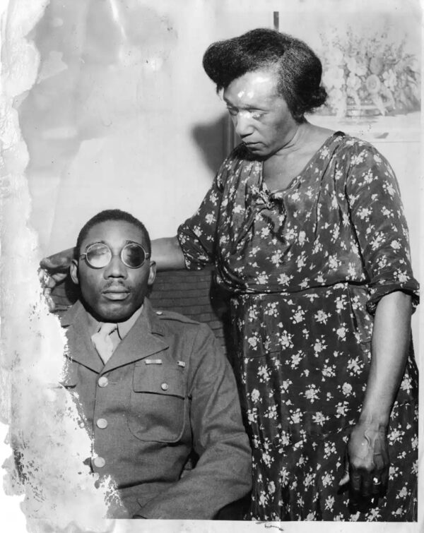 Black and white portrait of Isaac Woodard, in uniform wearing spectacles, seated next to his mother.